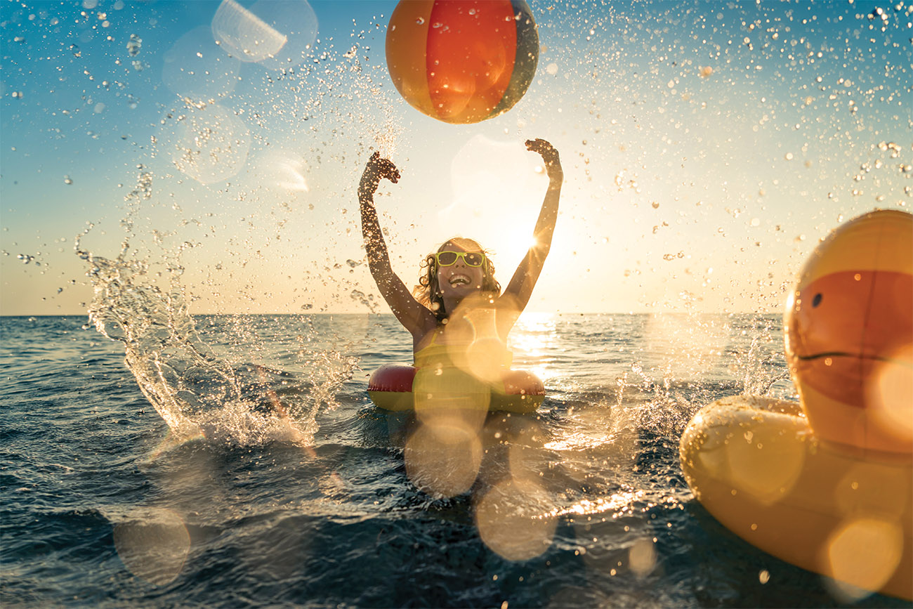 Happy child having fun on summer vacation. Kid playing with rubber duck and ball in the sea. Healthy lifestyle concept. Spring break!
