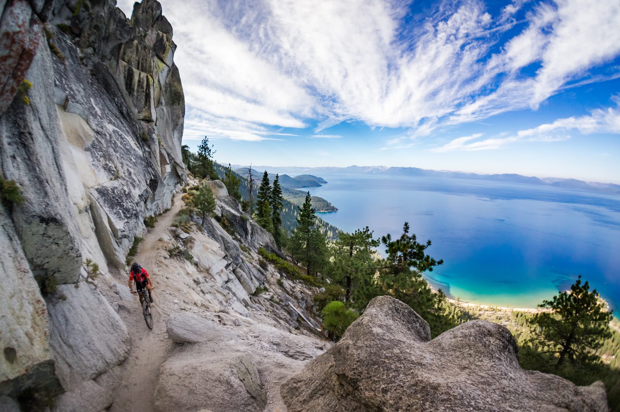 Mountain biker up on the mountain with evergreen trees and a deep blue lake below. 