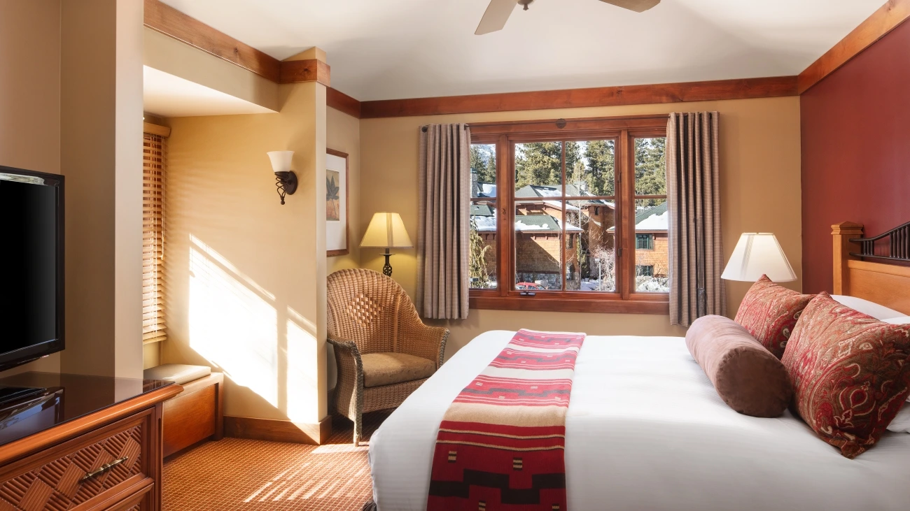 A bright bedroom with a window seat and windows looking over snow-topped buildings