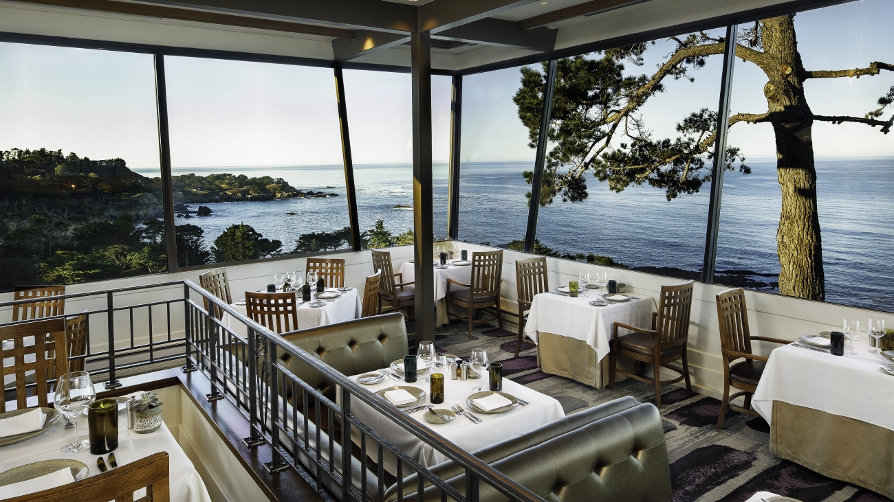 A restaurant with tables, and a wall of windows overlooking the ocean