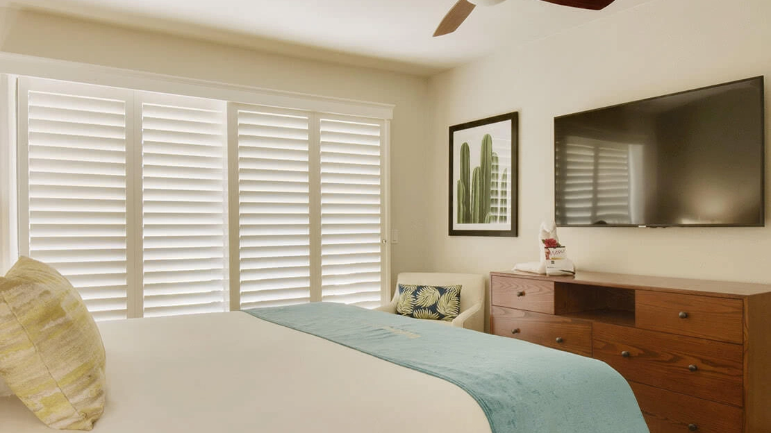 Villa bedroom with bed, armchair, dresser, HDTV, and framed cactus art on the wall