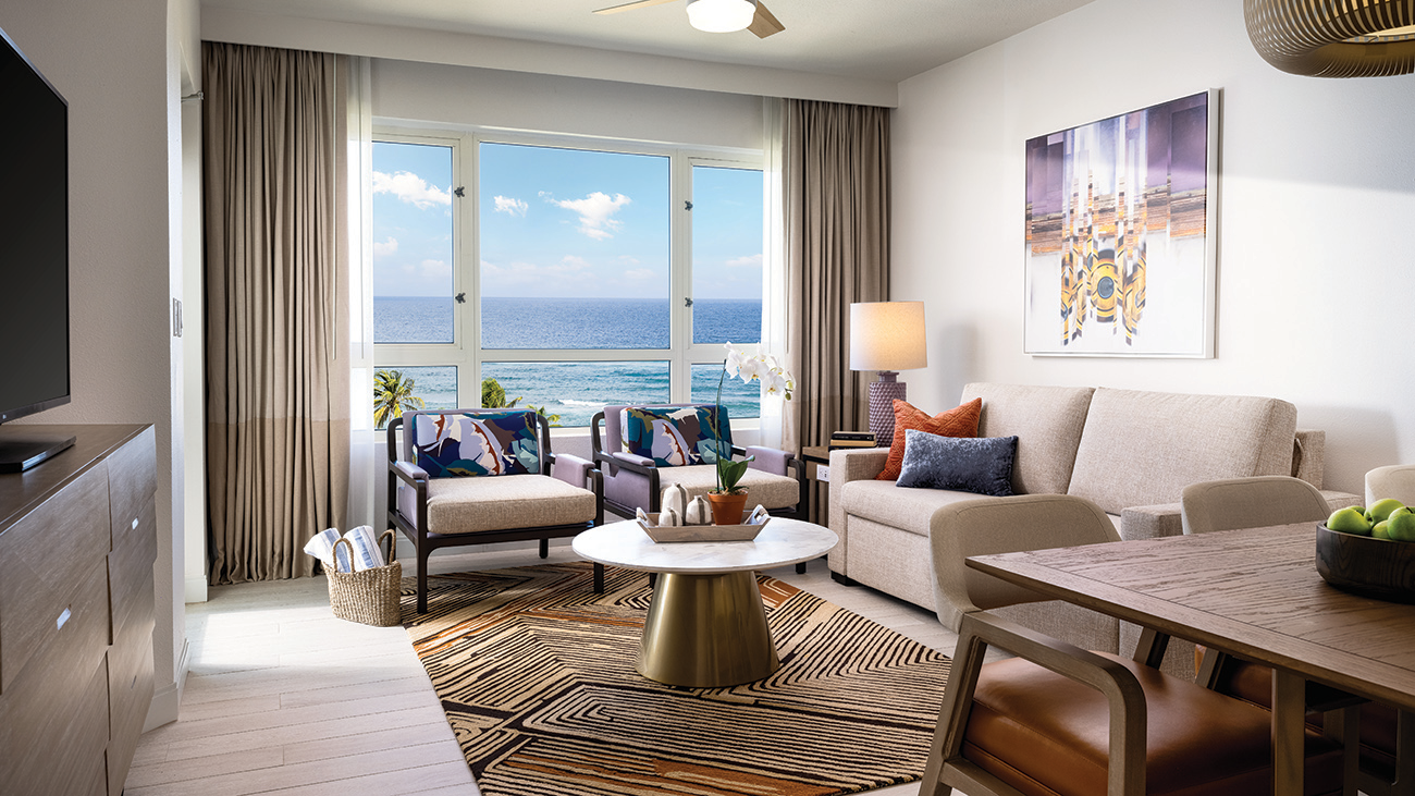 Deep purples line chairs and a couch of a bedroom as the ocean waves lap outside