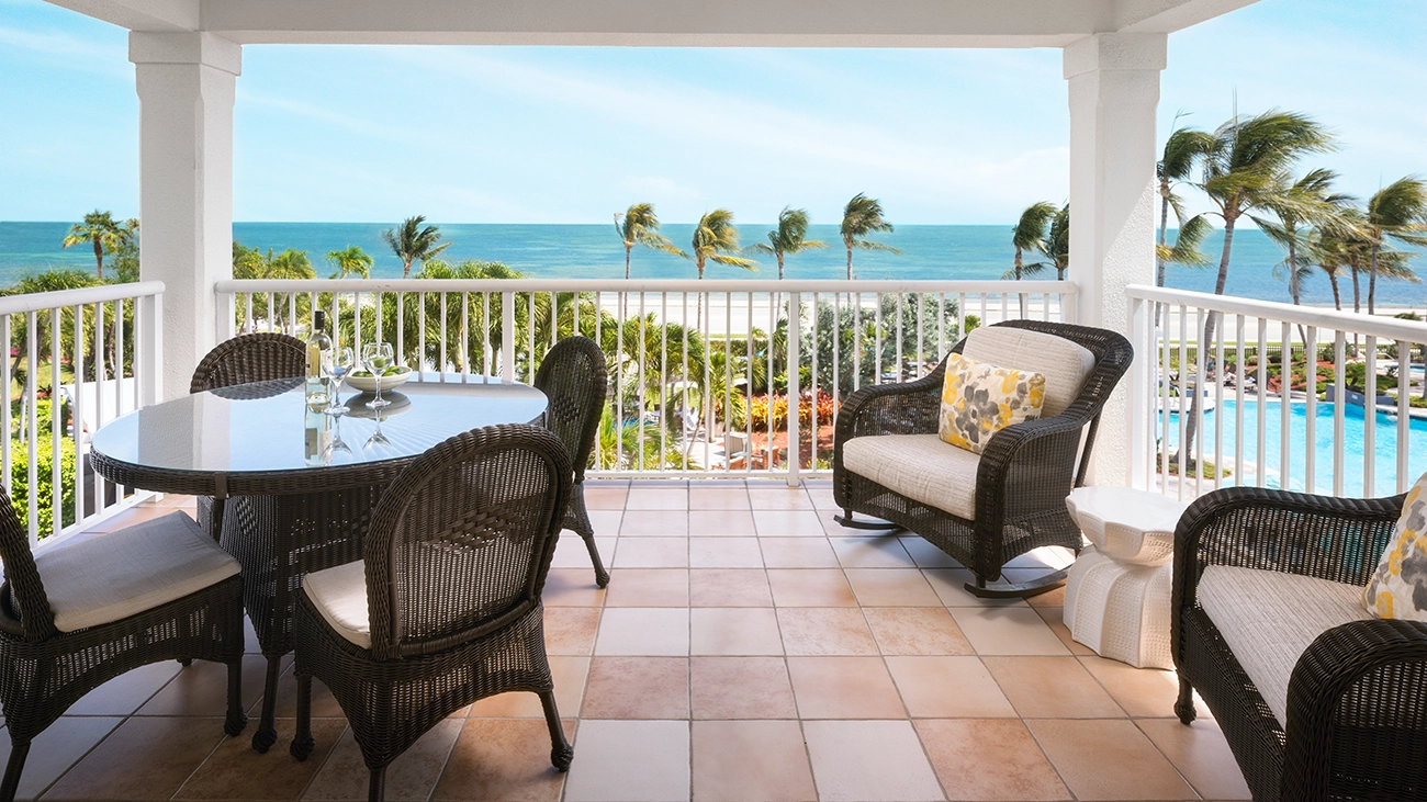 A dining table and rocking chairs sit on an outdoor patio overlooking the beach