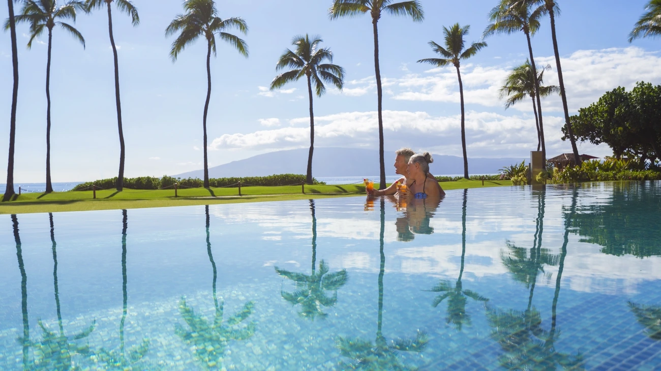 Couple enjoying tropical drinks as they relax in an infinity poop on Hawaii