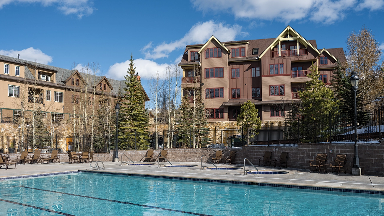 A large pool and a pair of hot tubs at Breckenridge Main Street Station sit under blue sky