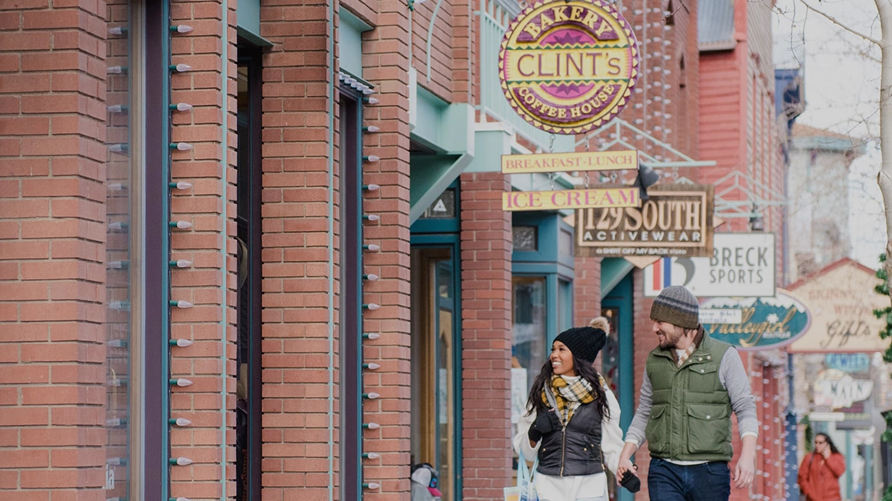 Couple wearing winter gear walking along a store-lined street