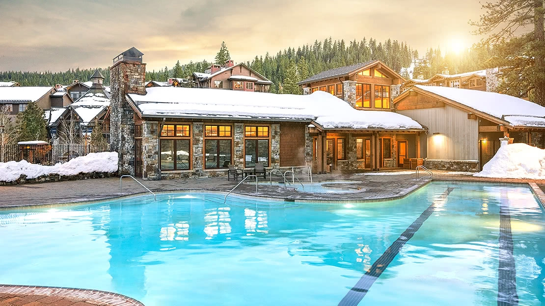 A glowing Northstar Lodge pool rests in front of the snow-capped resort
