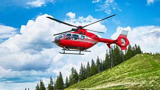 Red and white helicopter flying over an alpine landscape on a bright sunny day