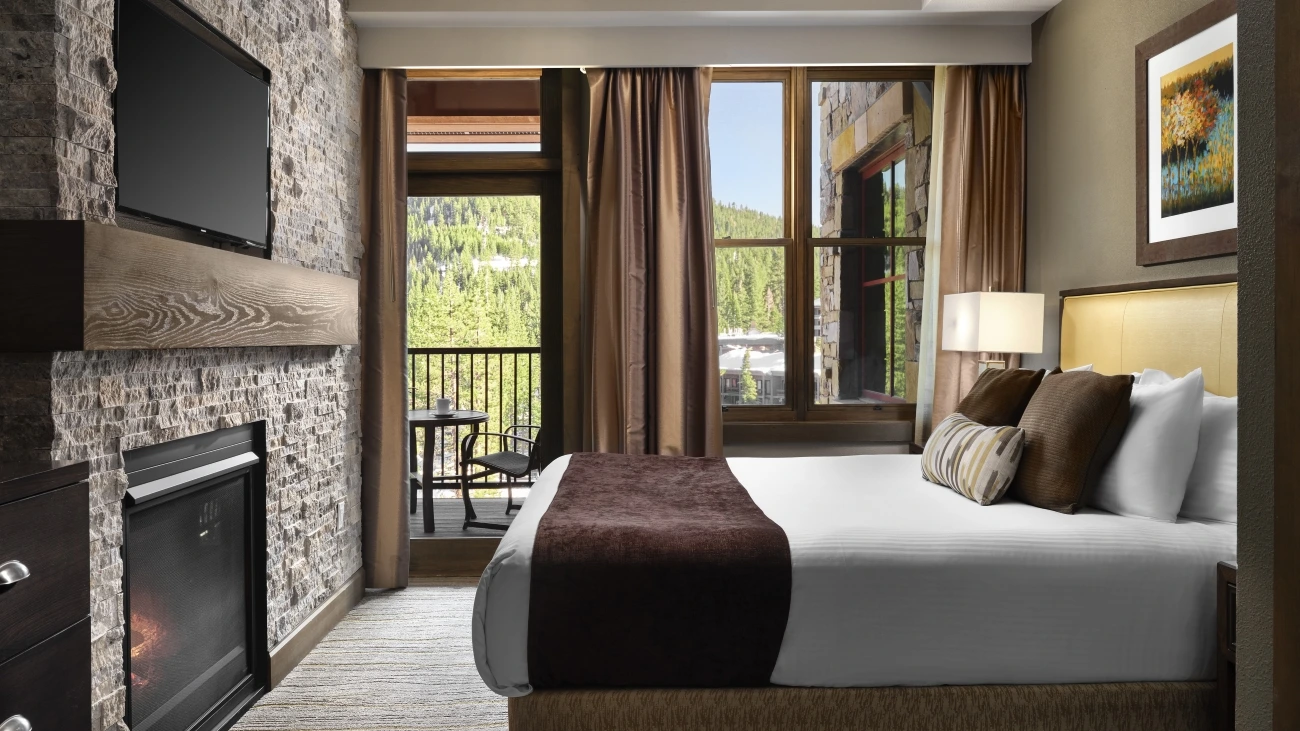 Interior view of villa bedroom with abed, armchair, and patio with a mountainous view