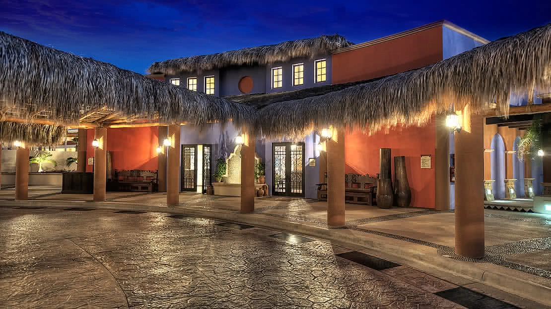 The front entrance of the resort lights up under a darkening sky