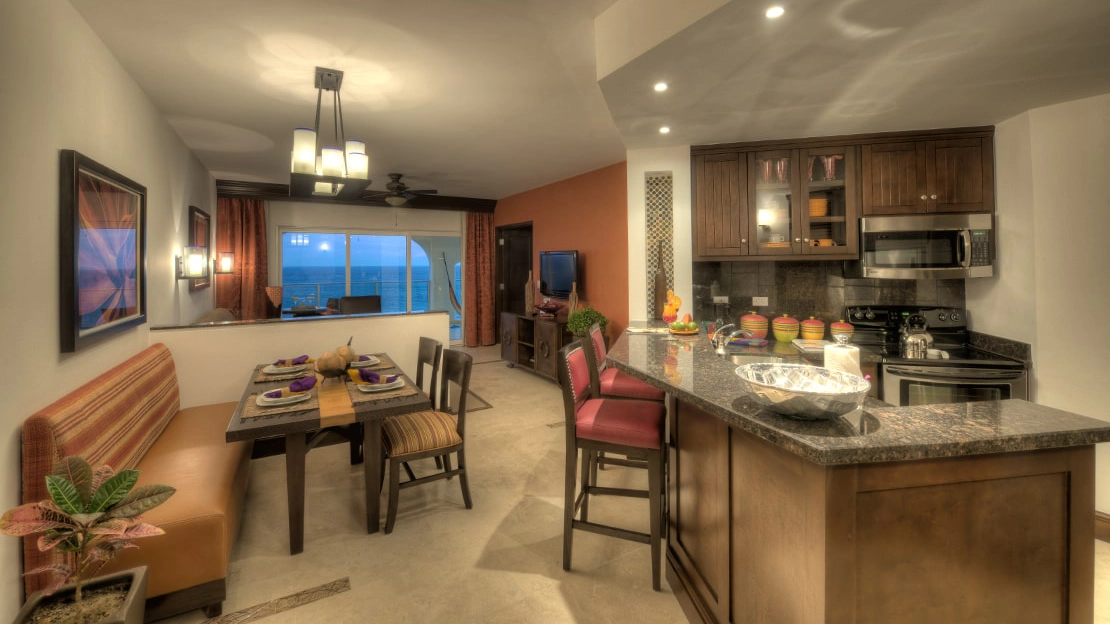Kitchenette with barstools, counter, and dining table, near a living room with ocean-view balcony 