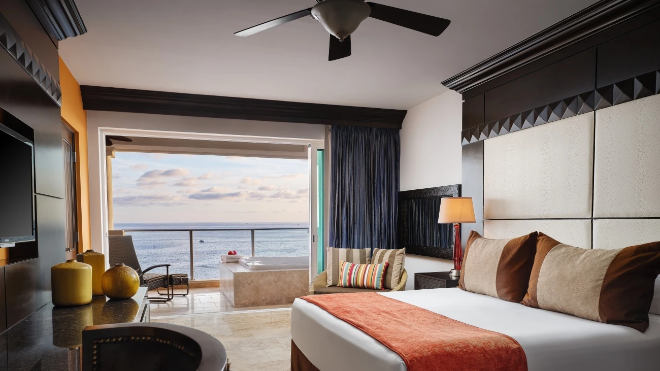 Room with bed and balcony with whirlpool spa, chairs, and ocean view