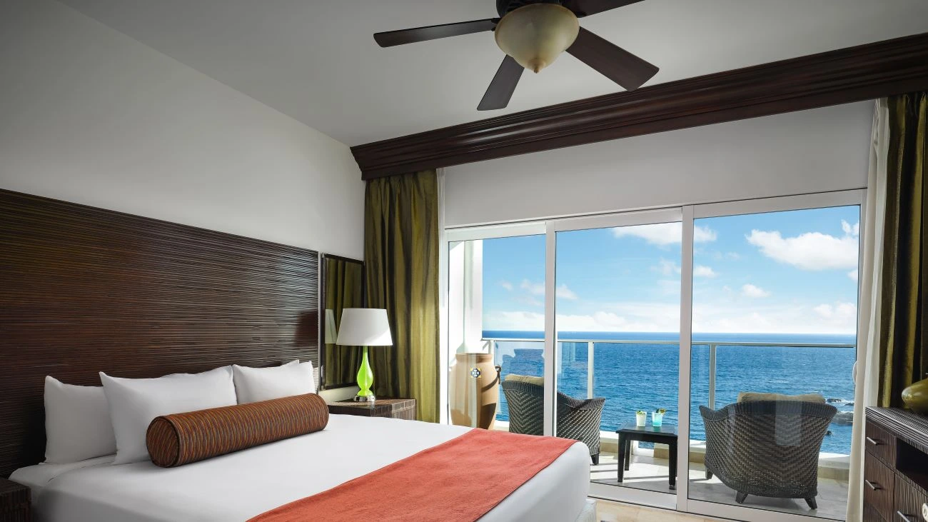 A bedroom with a balcony and chairs overlooking the ocean