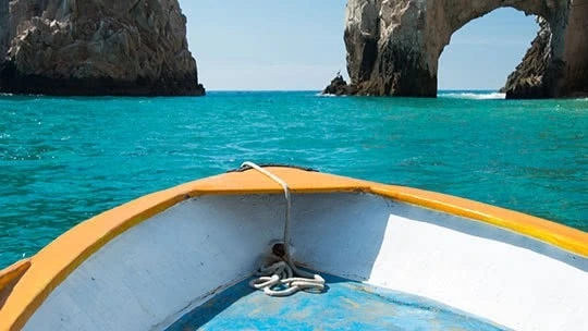 A boat on clear turquoise waters with a view of El Arco rock formation