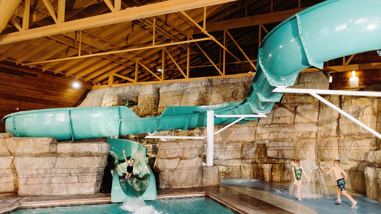 A girl goes down a slide and other children play in the water at the indoor water play area