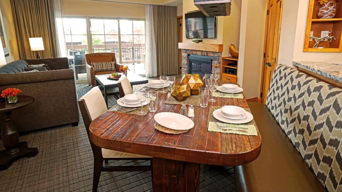 A rustic dining table and living room with a fireplace and balcony